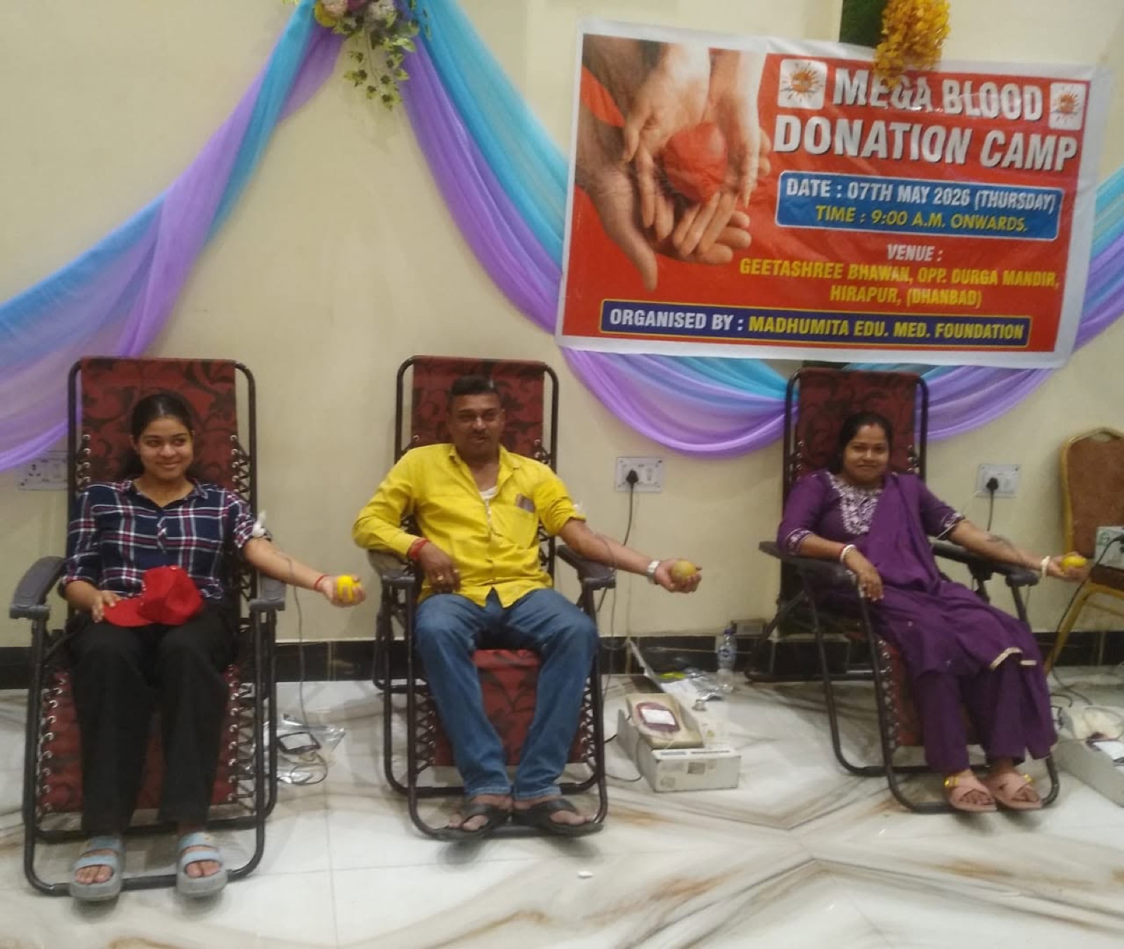 Three donors giving blood side by side beneath the MEM Foundation camp banner